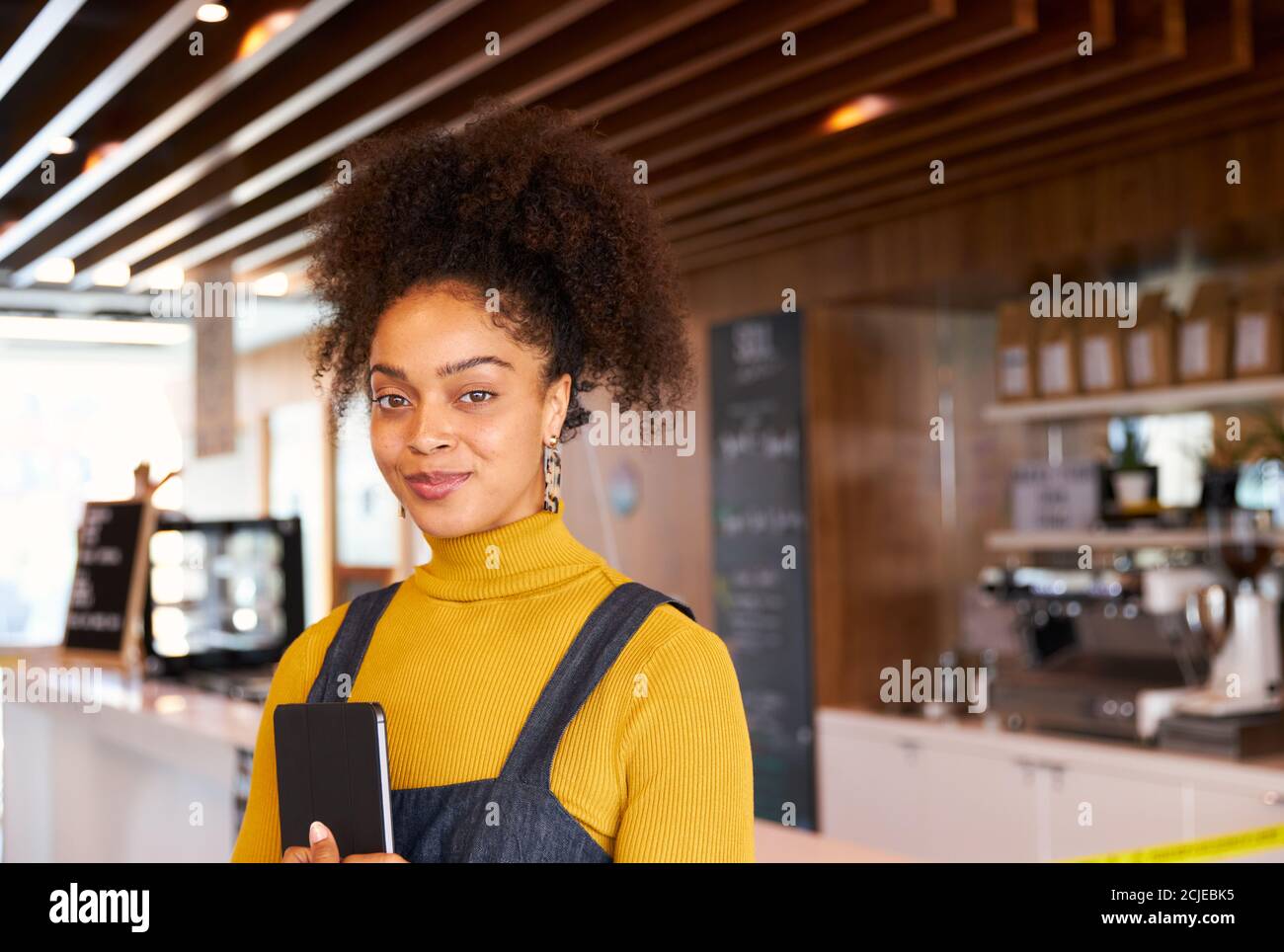 Portrait Of Female Business Owner Of Coffee Shop In Mask Using Digital Tablet During Health Pandemic Stock Photo