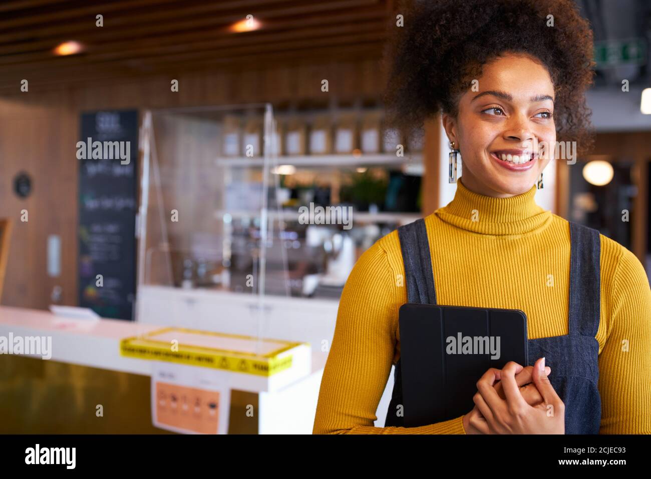 Portrait Of Female Business Owner Of Coffee Shop In Mask Using Digital Tablet During Health Pandemic Stock Photo