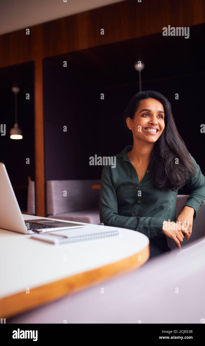 Businesswoman Sitting At Meeting Table Working On Laptop In Modern Open Plan Office Stock Photo