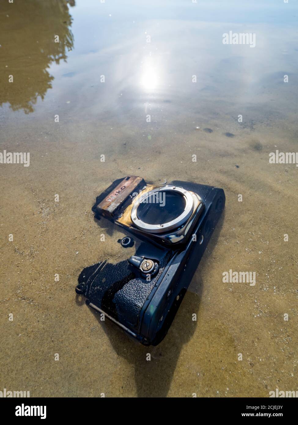 Nikon retro classic SLR film camera on beach sun bright reflection smooth calm sea water surface Stock Photo