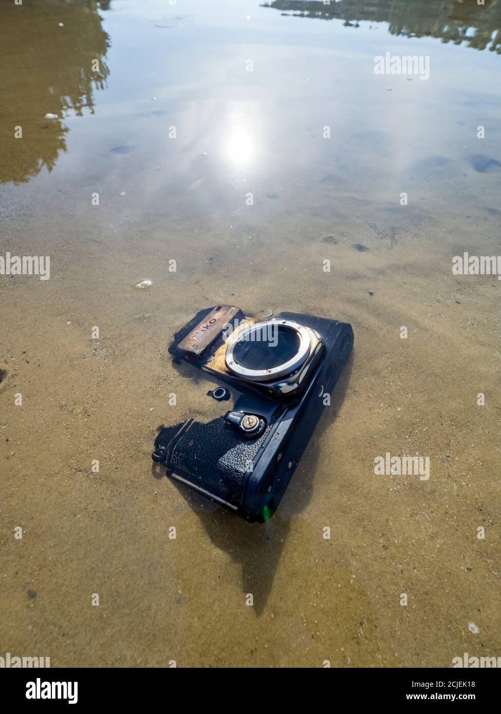 Nikon retro classic SLR film camera on beach sun bright reflection smooth calm sea water surface Stock Photo