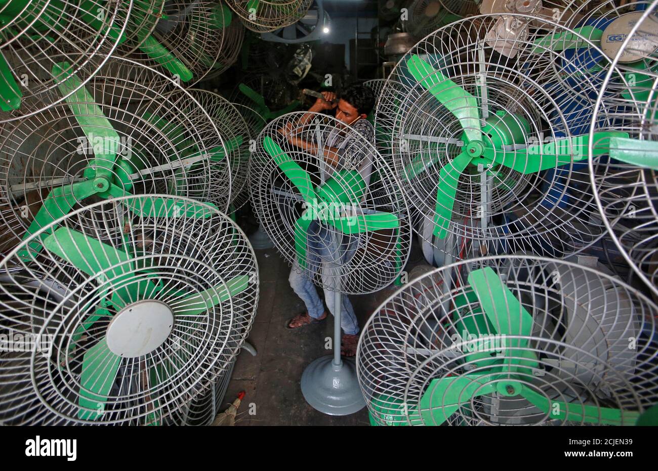 A mechanic uses a hammer to fix steel guard of an electric fan inside a shop in Mumbai, India, May 3, 2018. REUTERS/Francis Mascarenhas Stock Photo