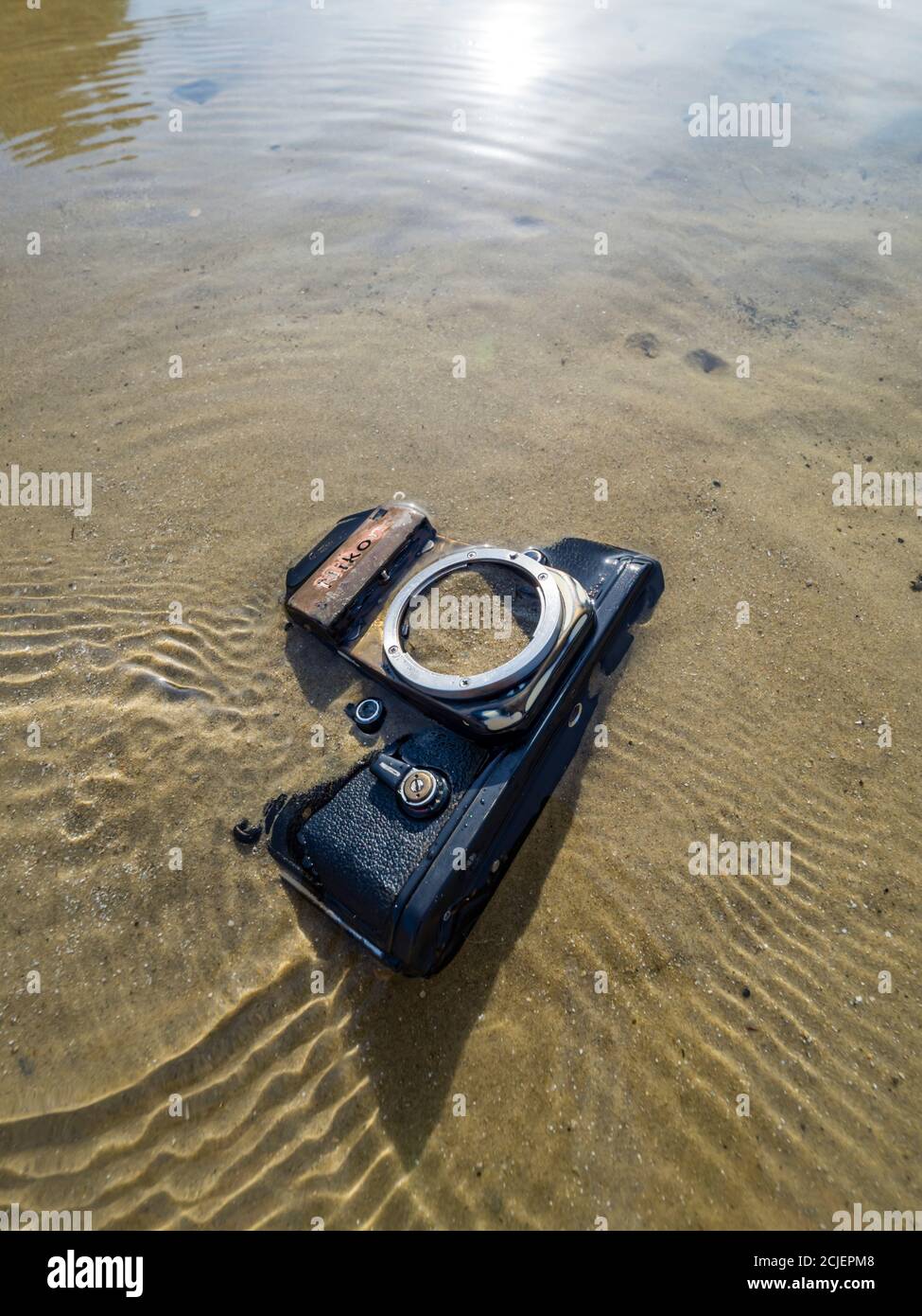 Nikon retro classic SLR film camera on beach sun bright reflection small ripples rippled sea water surface Stock Photo
