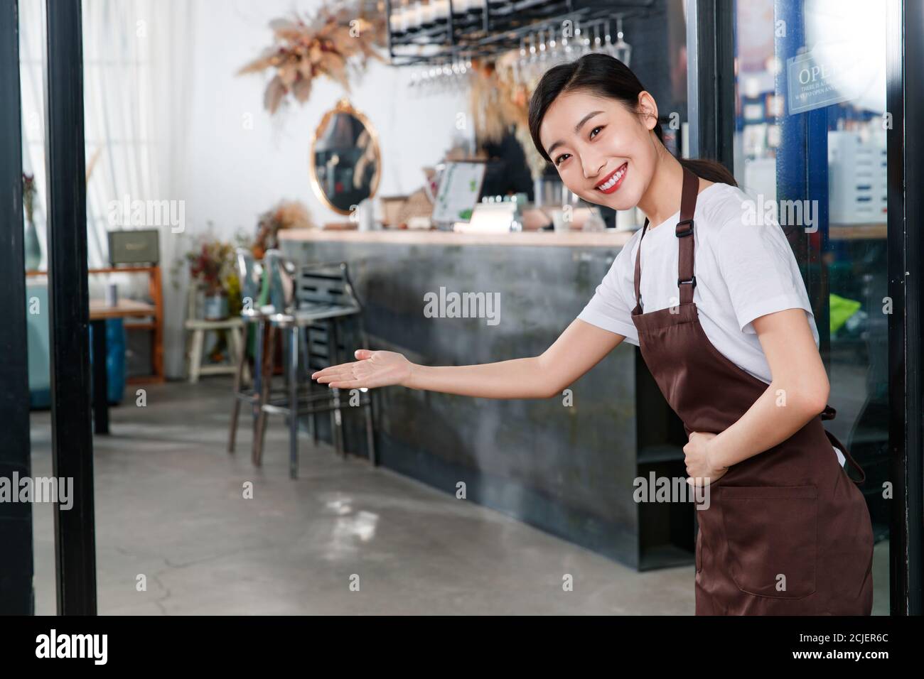 Standing a waitress in a coffee shop doorway do welcome gesture Stock Photo