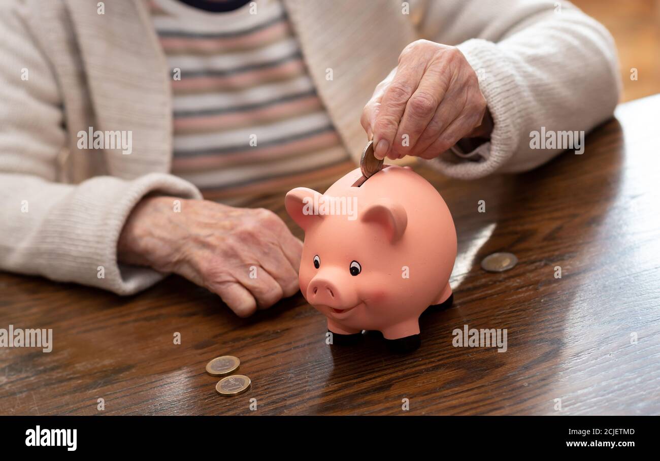 Elderly woman putting a coin in a piggy bank Stock Photo - Alamy