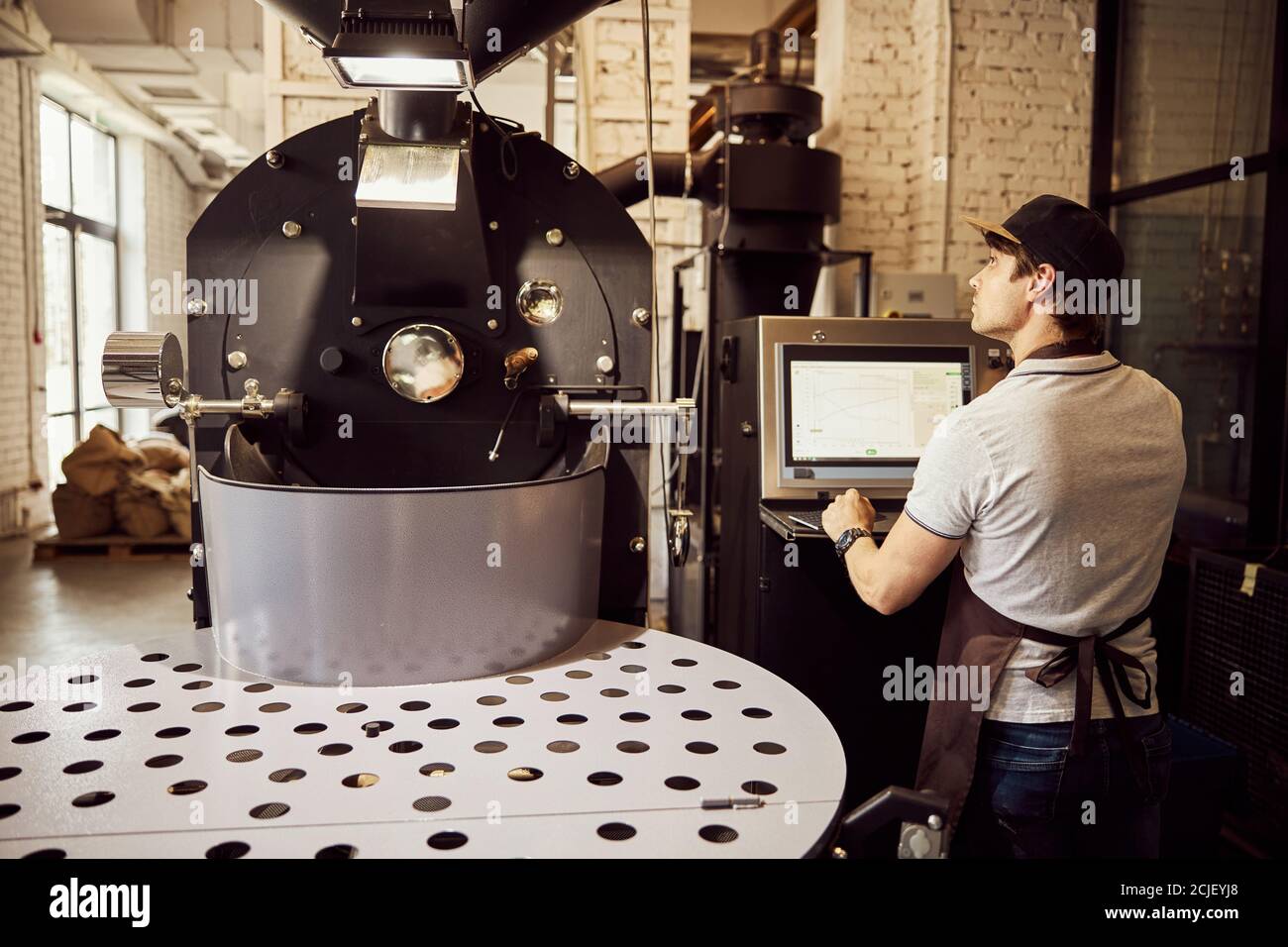 Professional male roaster using industrial coffee roasting machine