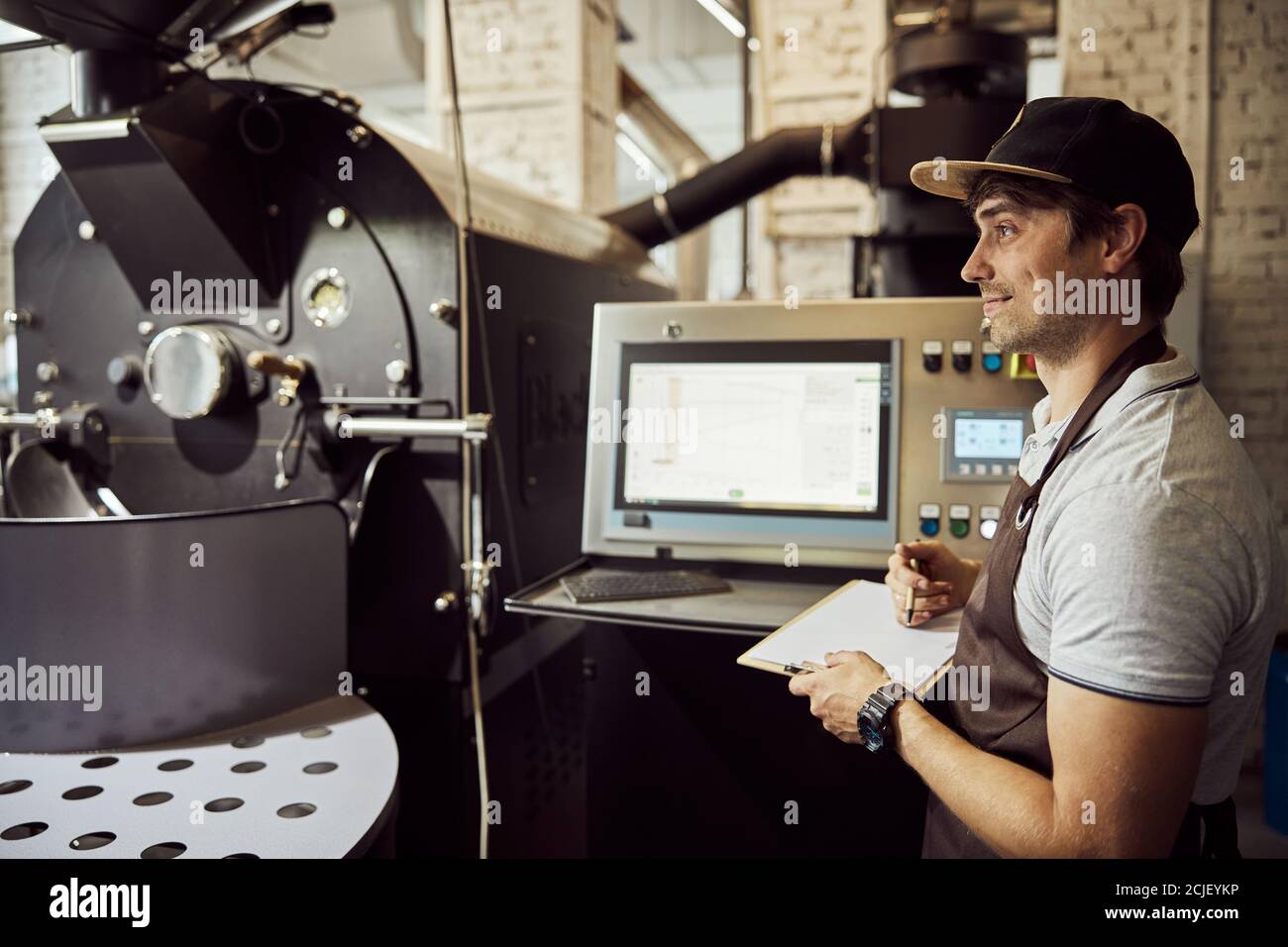 Handsome male worker using coffee roasting machine and taking notes Stock Photo