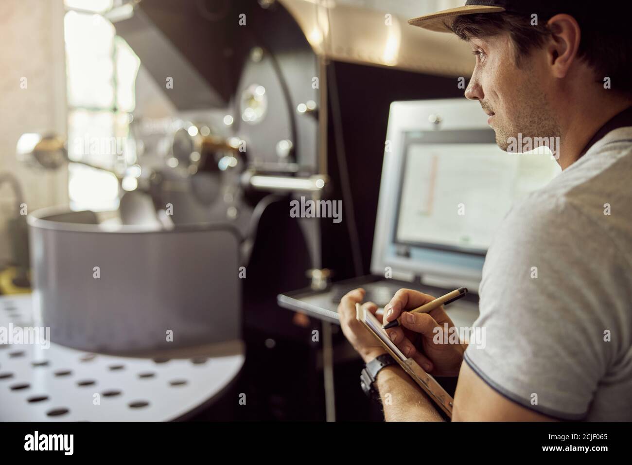 Male worker taking notes while using coffee roasting machine Stock Photo