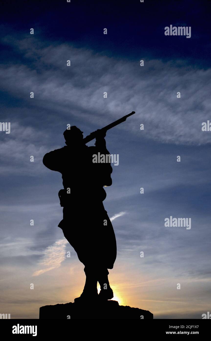 Bronze statue of a French rifleman or poilu silhouetted against the rising sun on the town monument at Monpazier in the Dordogne, Nouvelle-Aquitaine, France, to those who fell in the Franco-Prussian War of 1870-71. Stock Photo