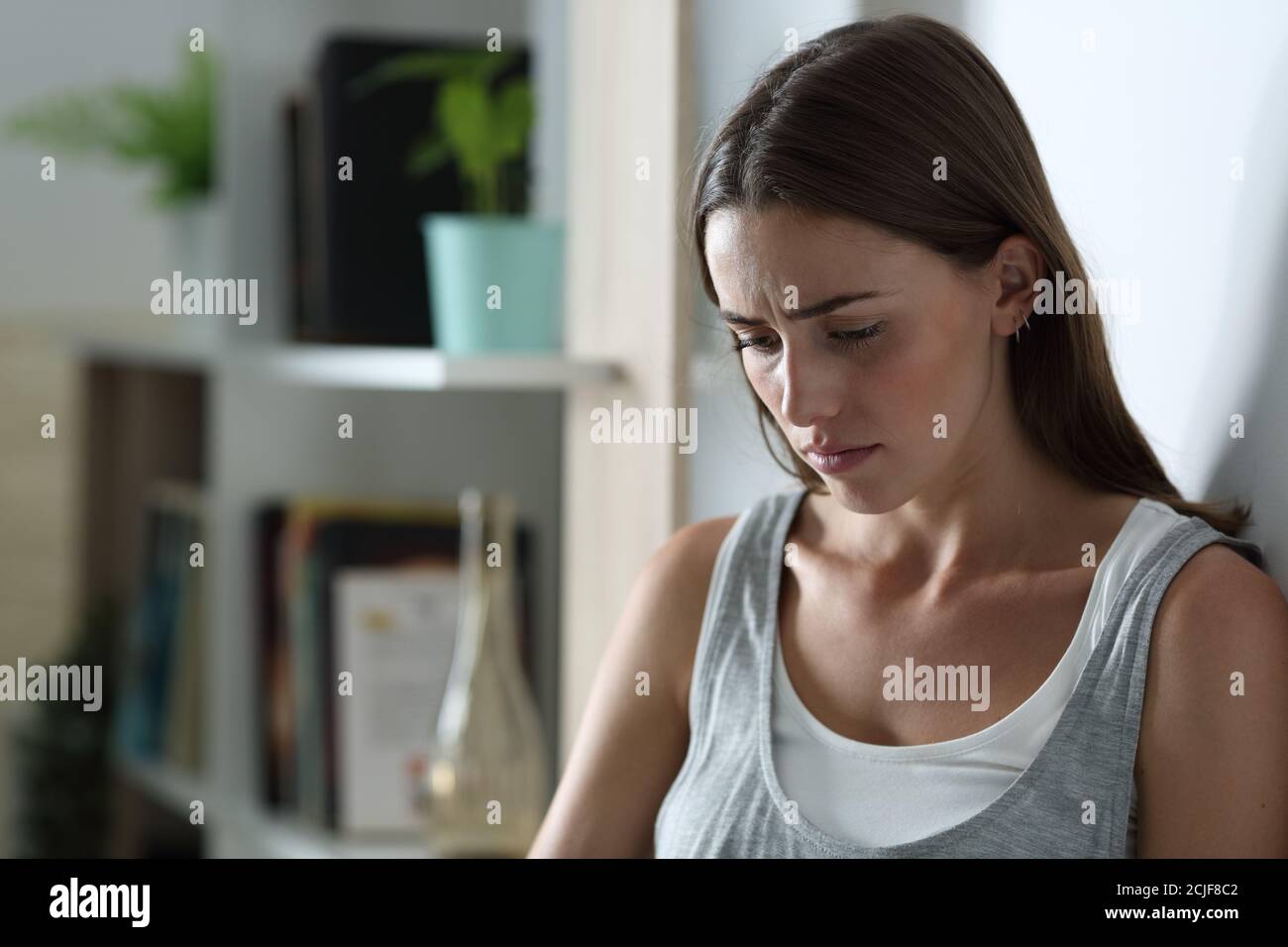 Sad girl complaining alone looking down at home in the night Stock Photo