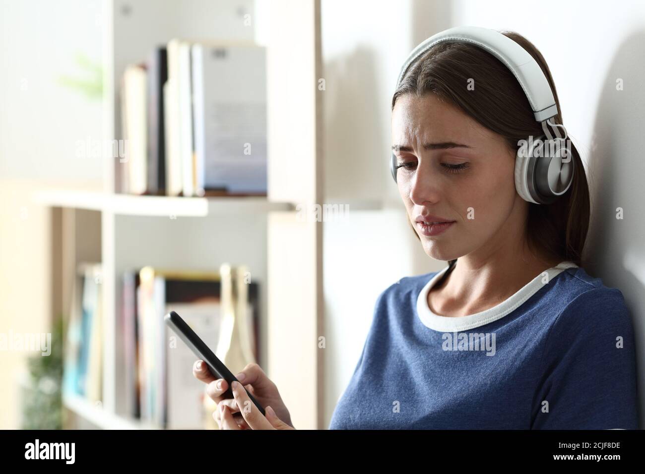 Sad teen complaining listening to music looking down and crying at home Stock Photo