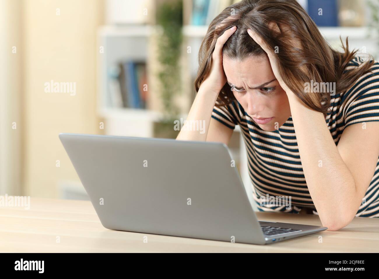 Worried teen checking laptop content on a desk at home Stock Photo