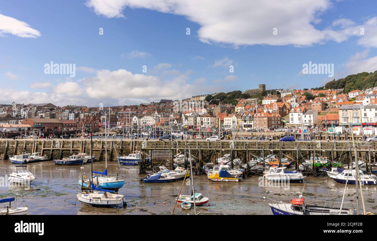 The harbour and town at Scarborough.  Boats are moored in the harbour with the shorefront behind.  House and buildings are stacked upwards from there Stock Photo