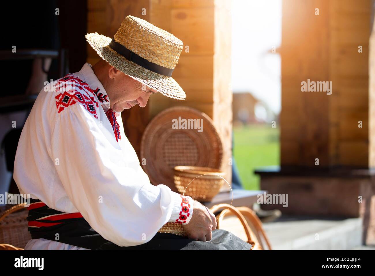 A Ukrinsky or Belarusian craftsman in embroidered shirt weaves baskets from birch bark. The man makes birch baskets. Stock Photo