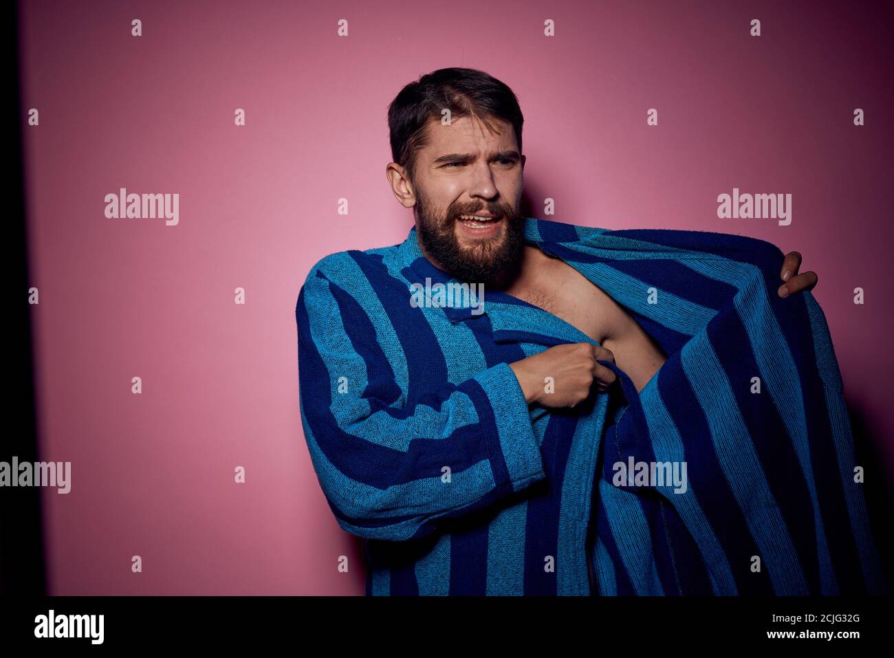 Bearded man in a blue striped robe on a pink background with hands ...