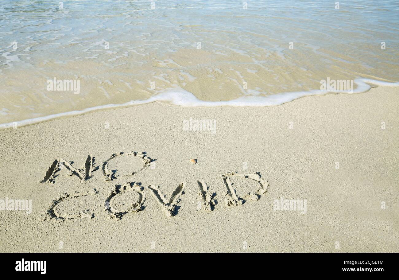"No covid" written on the sand of the shore of a beach with incoming waves. Fear of beach resort managers for the upcoming summer season due to the co Stock Photo