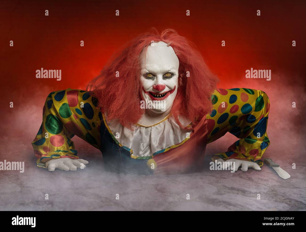 a scary clown with a knife is rising from the sewer in front of red ...