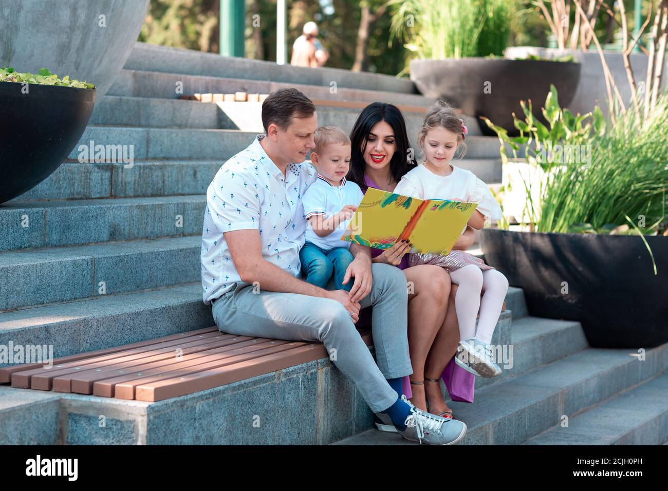 Happy young family with two kids sitting in the park reading a book. Happy parenting concept Stock Photo