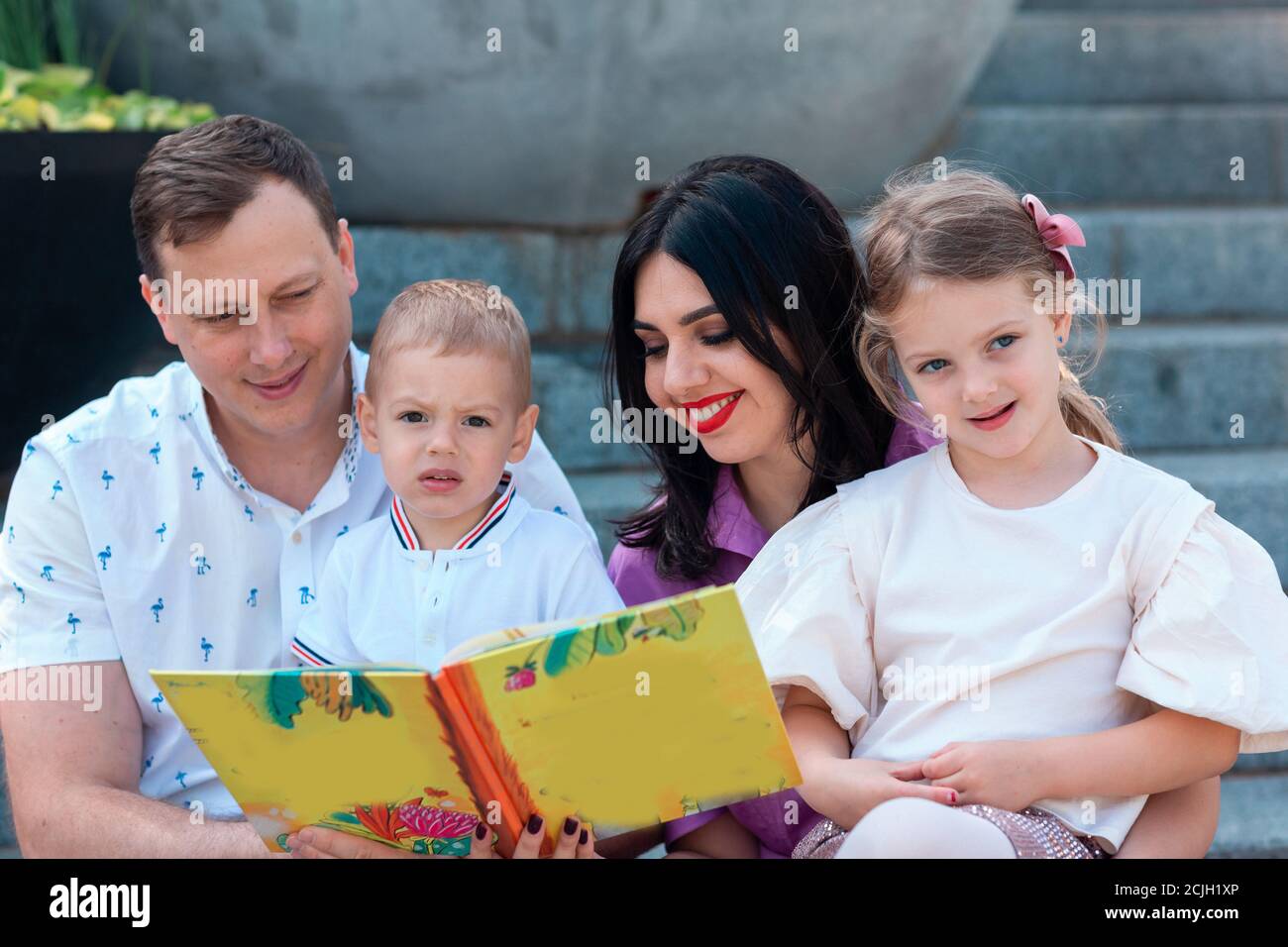 Happy young family with two kids sitting in the park reading a book. Happy parenting concept Stock Photo