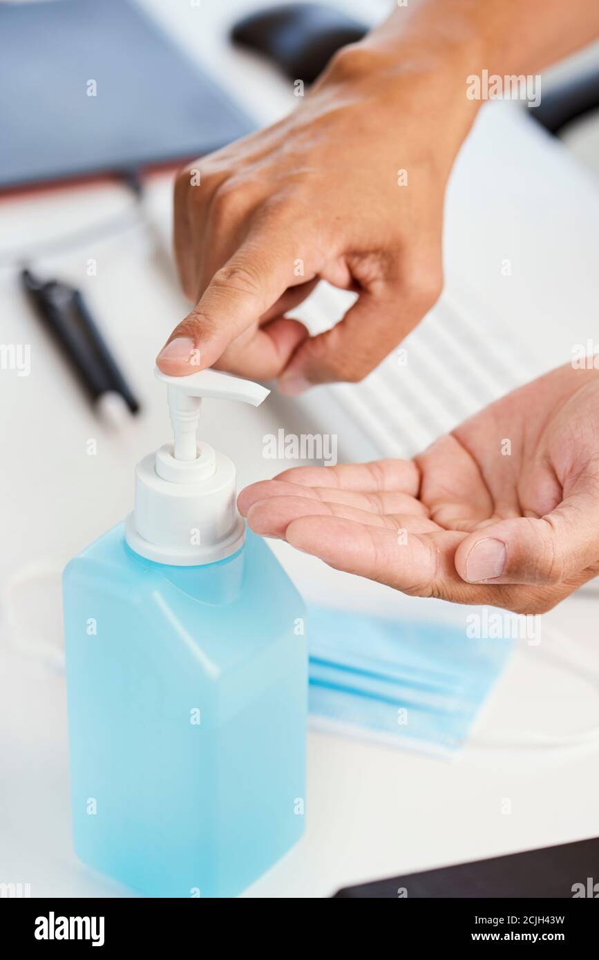 closeup of a young caucasian man disinfecting his hands with hand sanitizer, sitting at his office desk Stock Photo