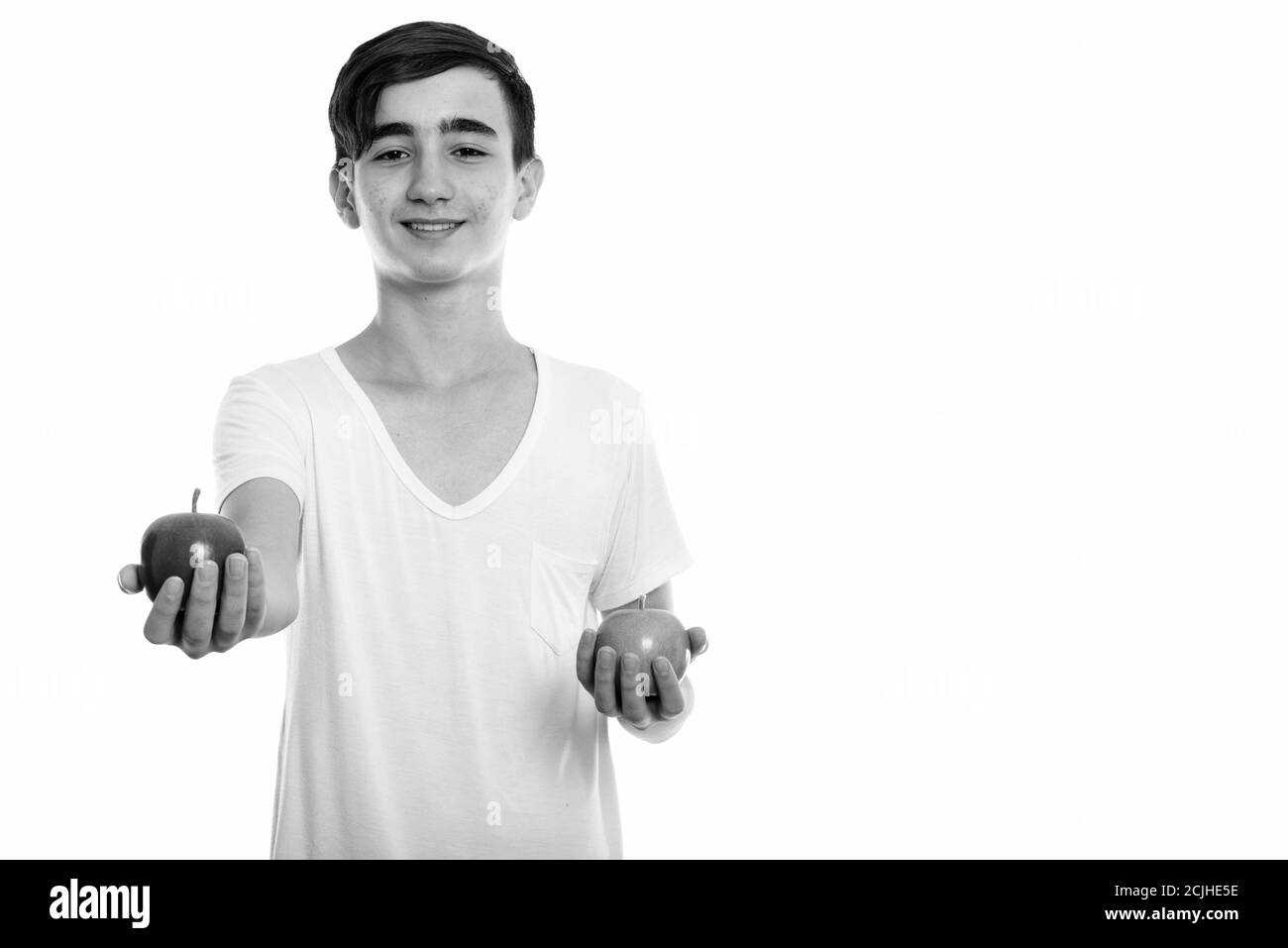 Studio shot of young happy Persian teenage boy smiling while giving red ...