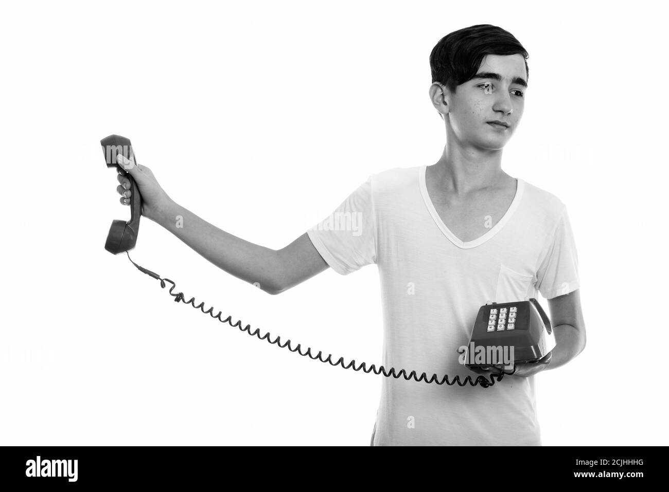 Studio shot of young stressed Persian teenage boy holding old telephone away Stock Photo
