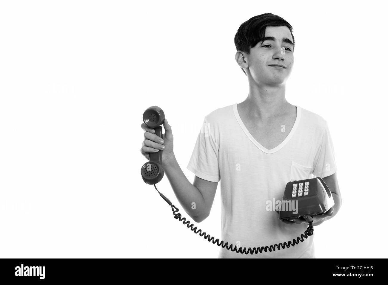 Studio shot of young handsome Persian teenage boy holding old telephone while looking annoyed Stock Photo