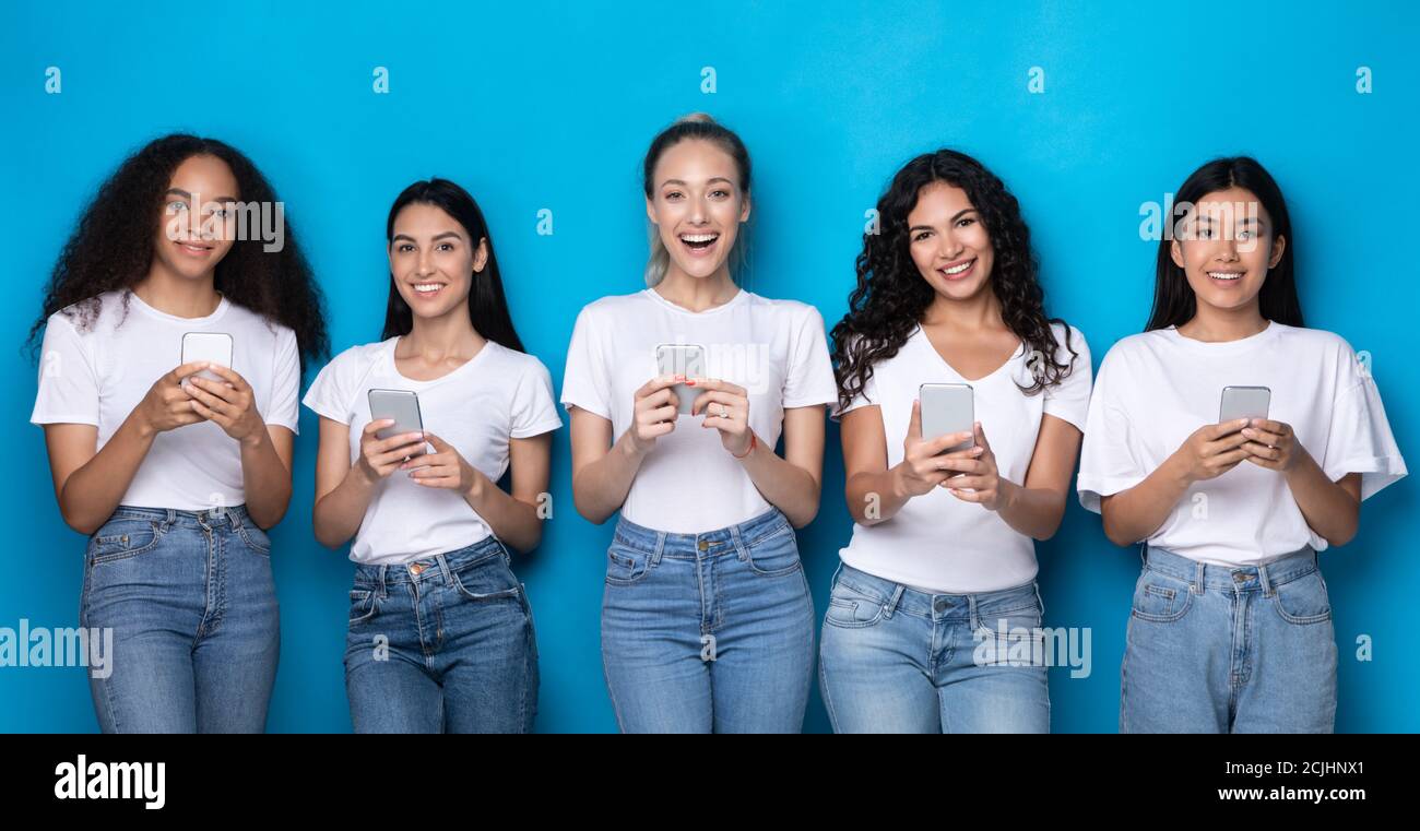 Five Multiracial Women Using Smartphones Over Blue Studio Background, Panorama Stock Photo
