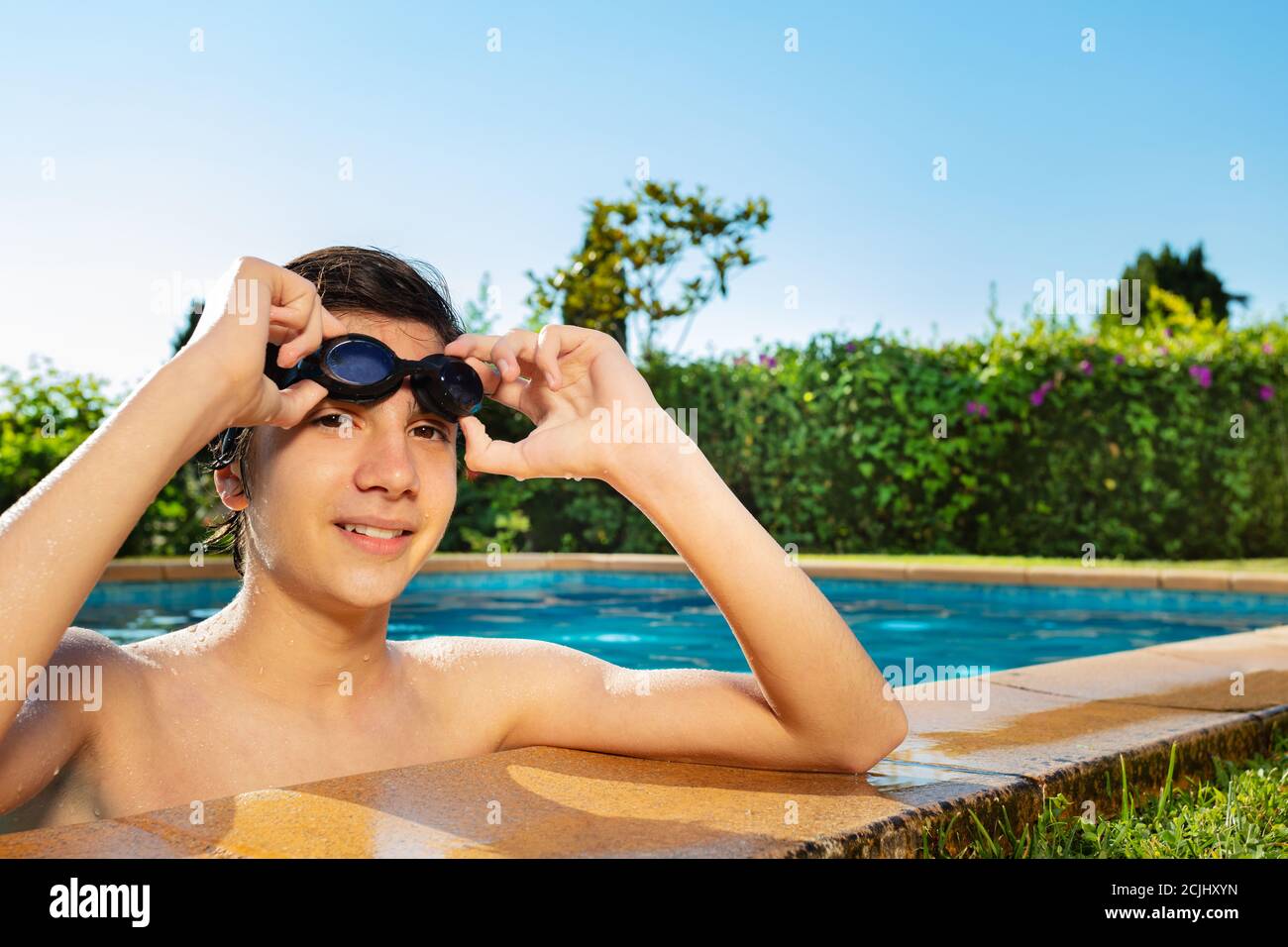 Happy handsome boy on the border of swimming pool hold in hands swim