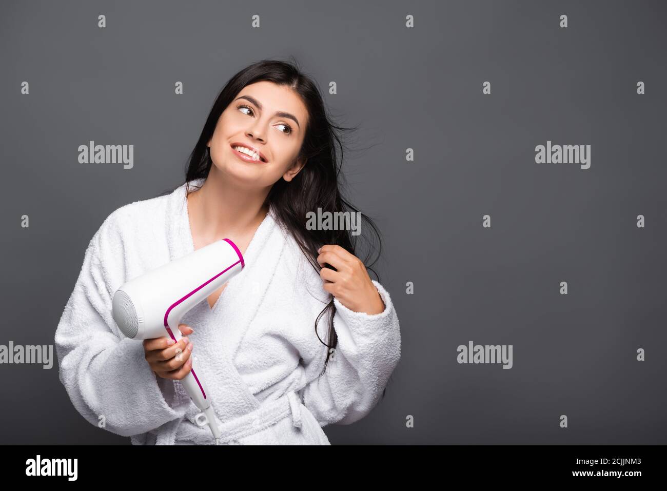 brunette long haired woman in bathrobe using hairdryer isolated on black Stock Photo