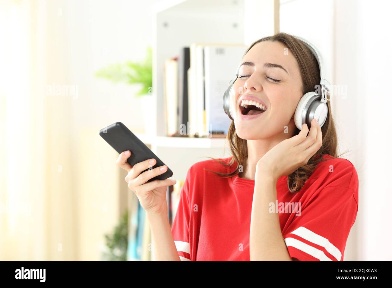 Happy teen wearing headphones singing listening to music on smart