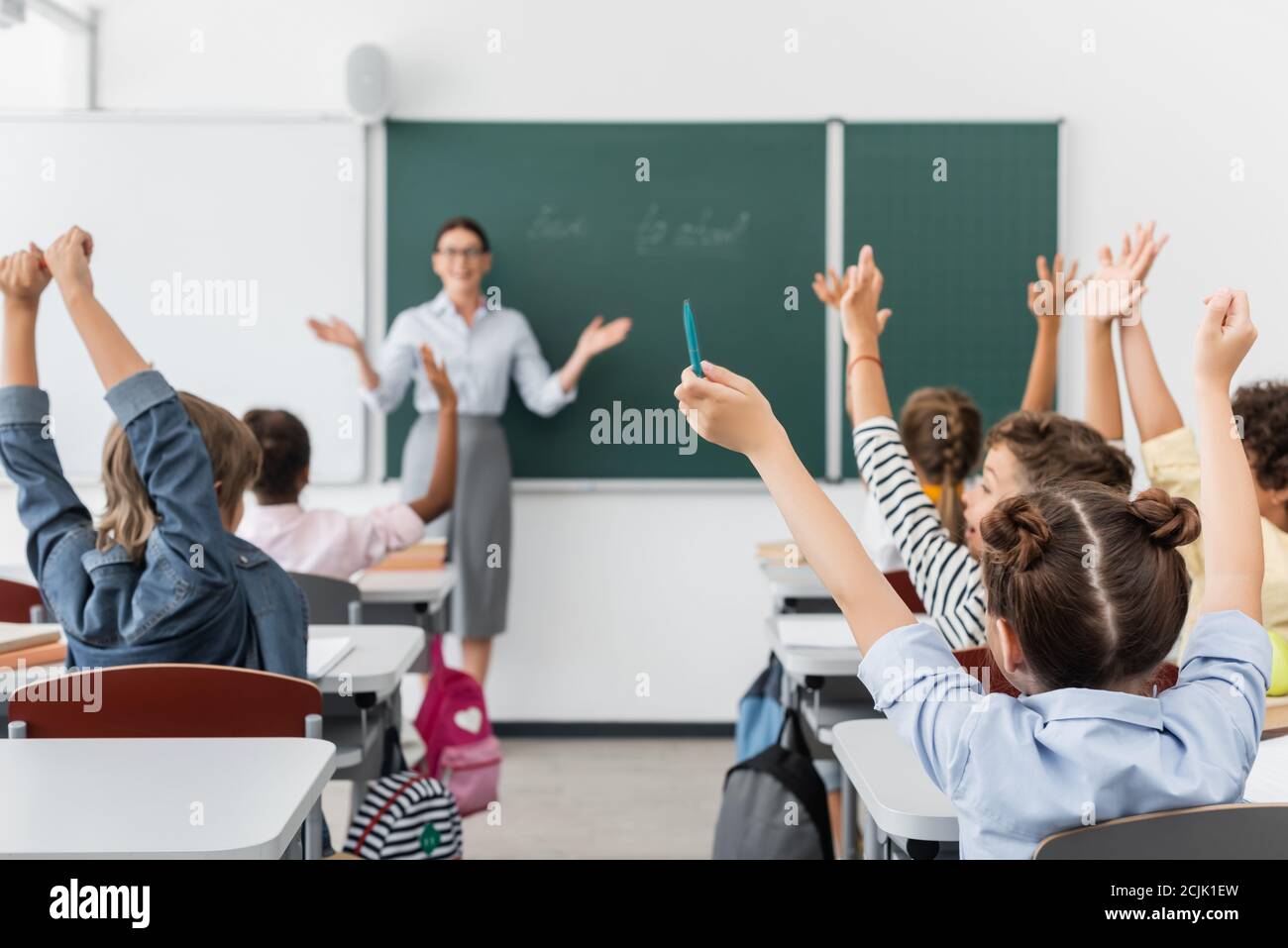 back view of multicultural pupils with hands in air, and teacher