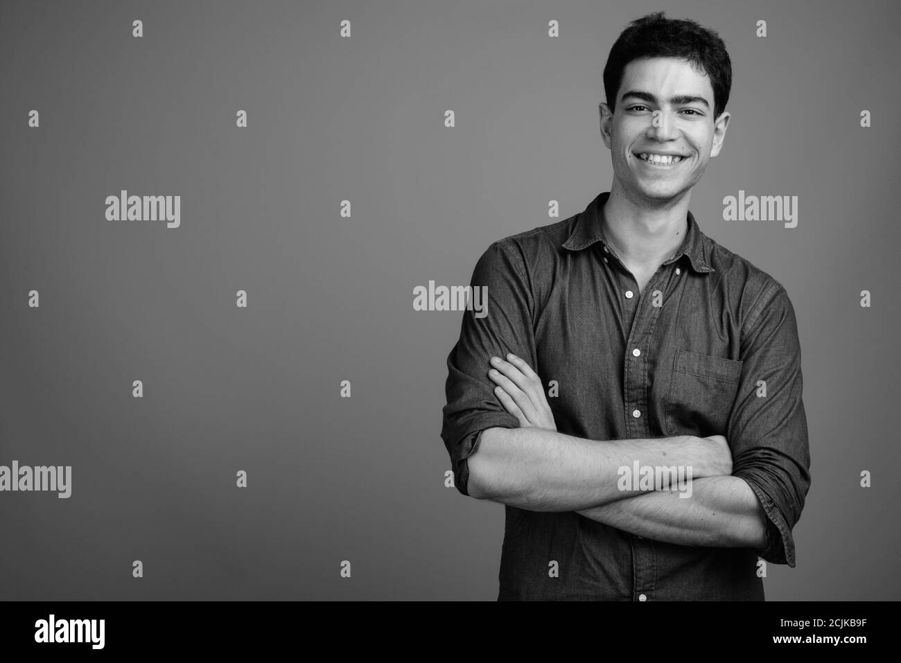 Portrait of happy young handsome Persian businessman smiling with arms ...