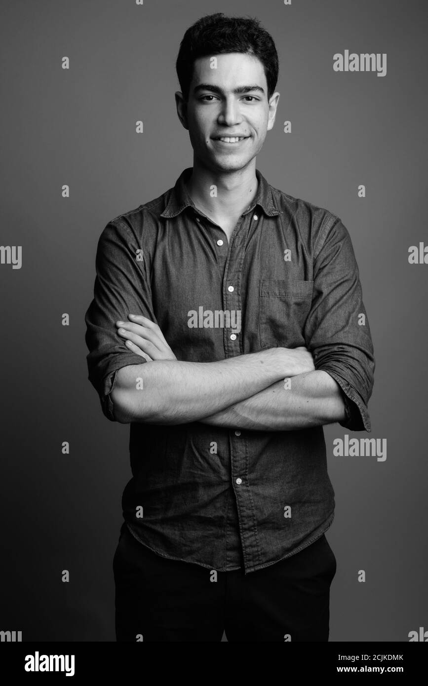 Portrait of happy young handsome Persian businessman smiling with arms ...