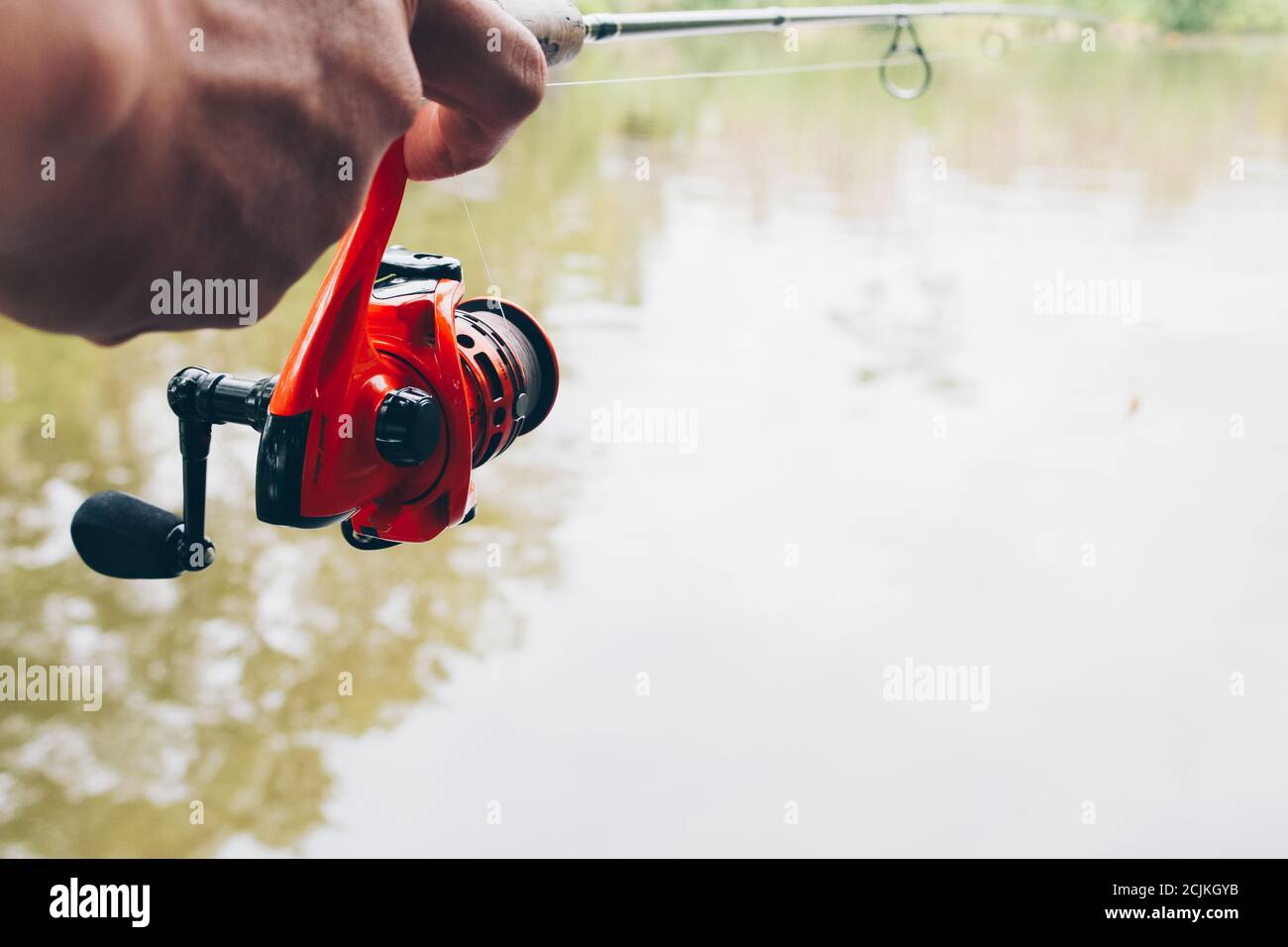 https://c8.alamy.com/comp/2CJKGYB/close-up-of-spinning-with-the-fishing-reel-in-the-hand-fishing-hook-on-the-line-with-the-bait-in-the-left-hand-against-the-background-of-the-water-2CJKGYB.jpg