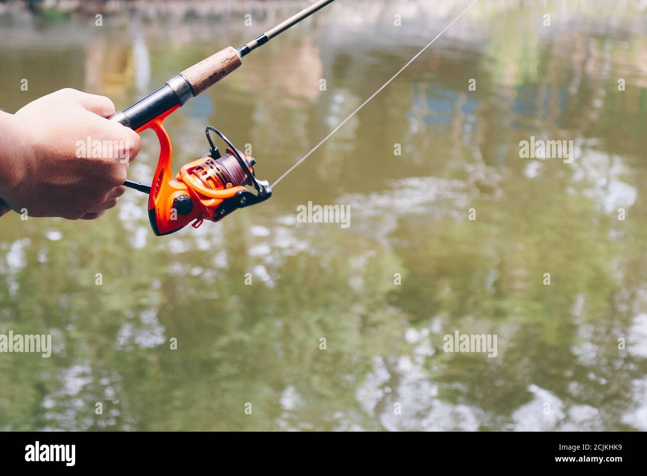 Close up of spinning with the fishing reel in the hand, fishing hook on the  line with the bait in the left hand against the background of the water  Stock Photo 