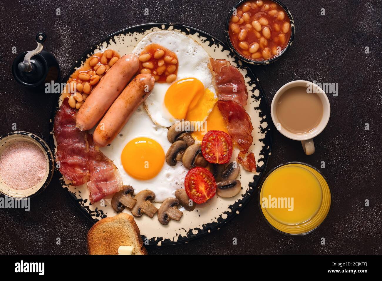 English traditional breakfast on a dark brown rustic background. Top view, flat lay, copy space. Fried eggs with bacon, sausages and beans, coffee, or Stock Photo