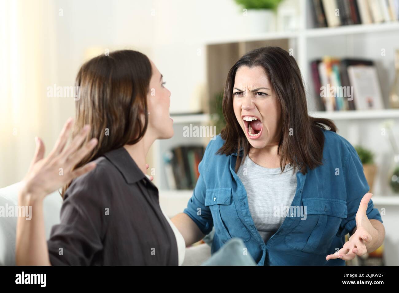 Two roommates arguing and shouting on a couch in the living room at home Stock Photo