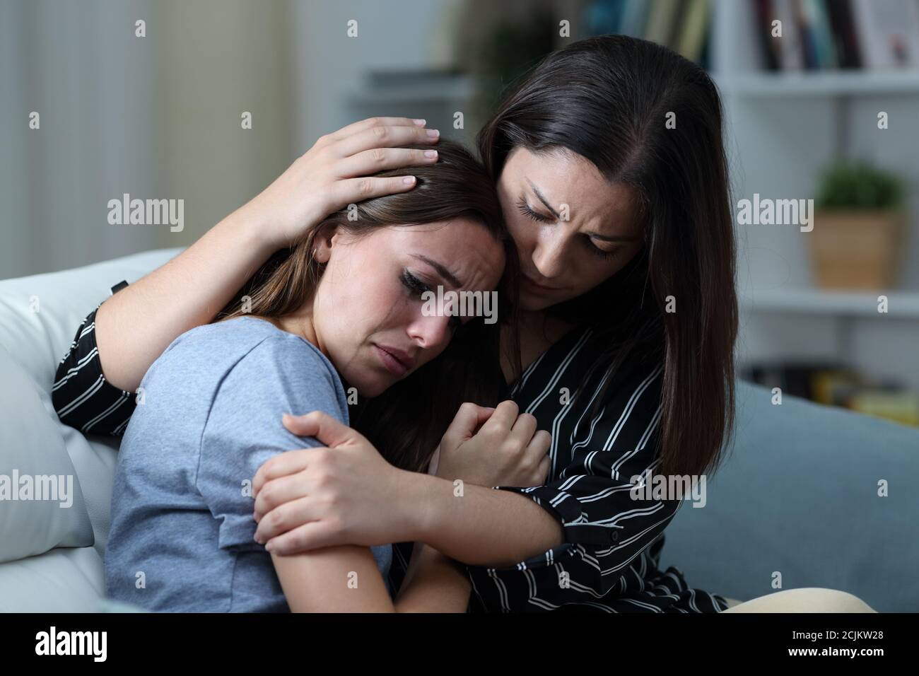 Sad teen crying being comforted by her sister on a couch in the living room at home Stock Photo