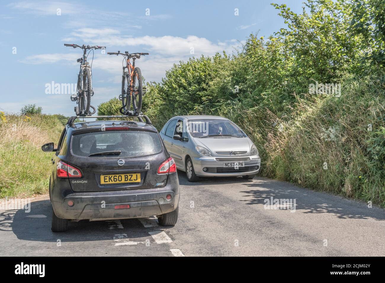 Cornish country road & car with cycle car rack and bicycles mounted on the roof. For UK staycation Cornwall, cycling holiday, cycling enthusiasts. Stock Photo