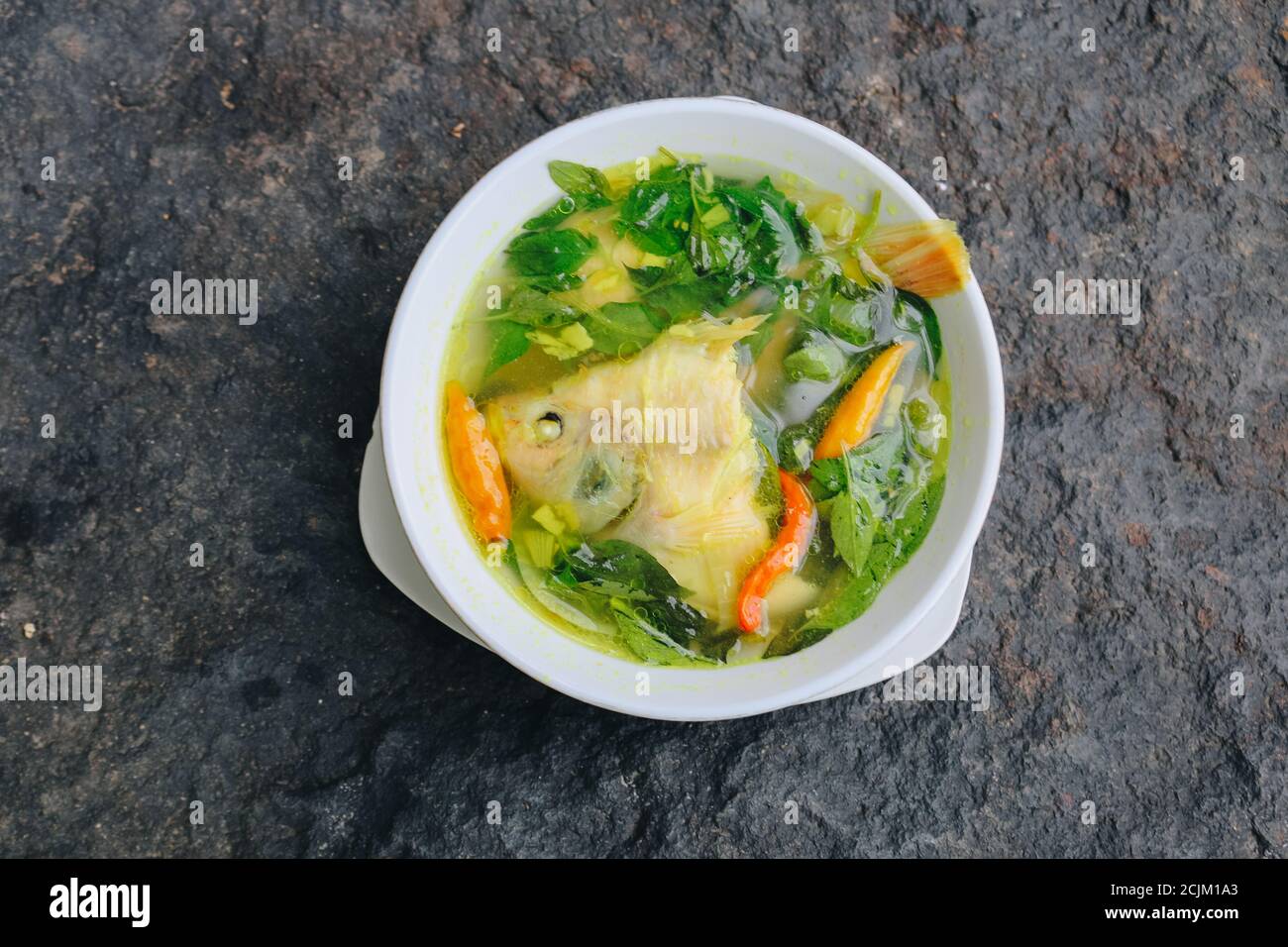 Gurame fish head soup or sup kepala ikan gurame with basil leaves, tomatoes, yellow curry, and chilli in a bowl. Indonesian food Stock Photo