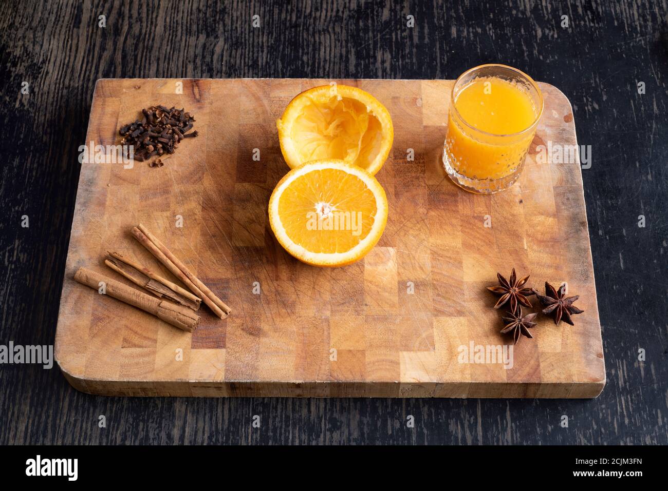 Spiced orange – a fresh cut and squeezed glass of orange juice with aromatic spices cinnamon, cloves and star anise on a wooden cutting board Stock Photo