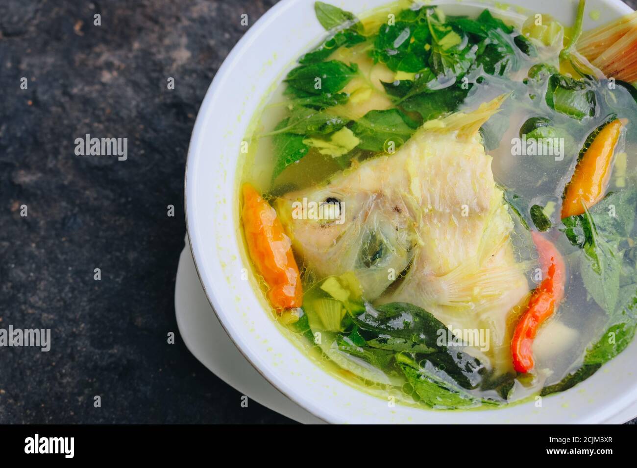 Gurame fish head soup or sup kepala ikan gurame with basil leaves, tomatoes, yellow curry, and chilli in a bowl. Indonesian food Stock Photo