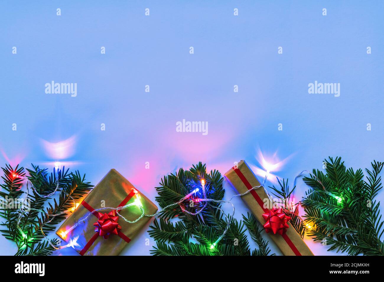 Boxes with gift and Christmas fir twigs, garland with colorful lights, neon color background. Top view, flat lay, copy space. Stock Photo