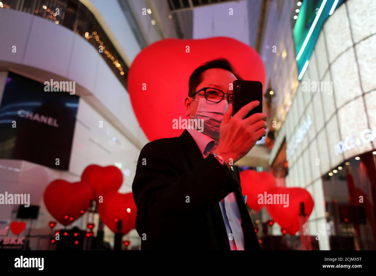 A man wearing a face mask takes a selfie in front of hearts celebrating  Valentine's Day