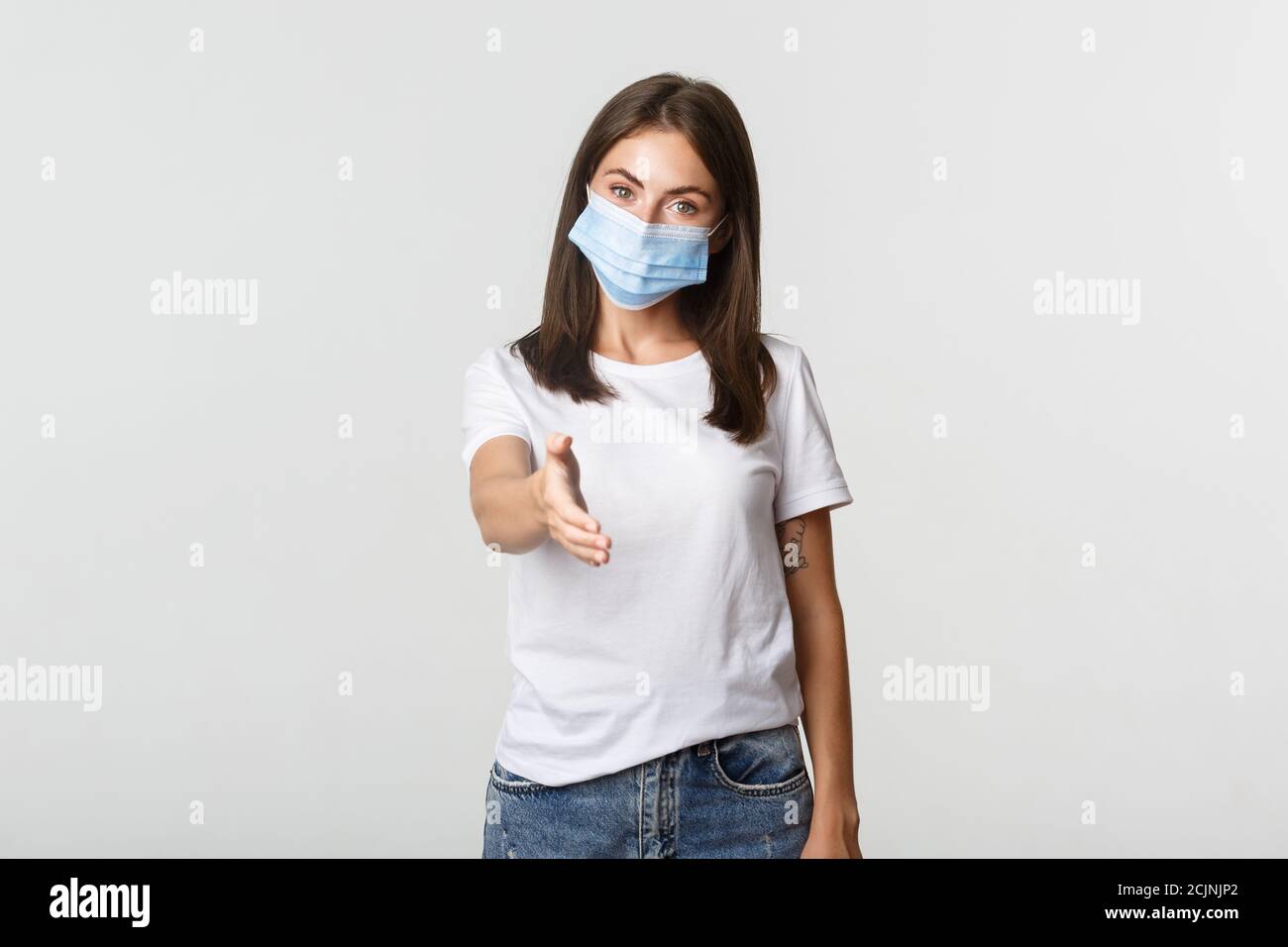 Covid-19, health and social distancing concept. Portrait of friendly attractive young woman in medical mask, extending hand for handshake Stock Photo