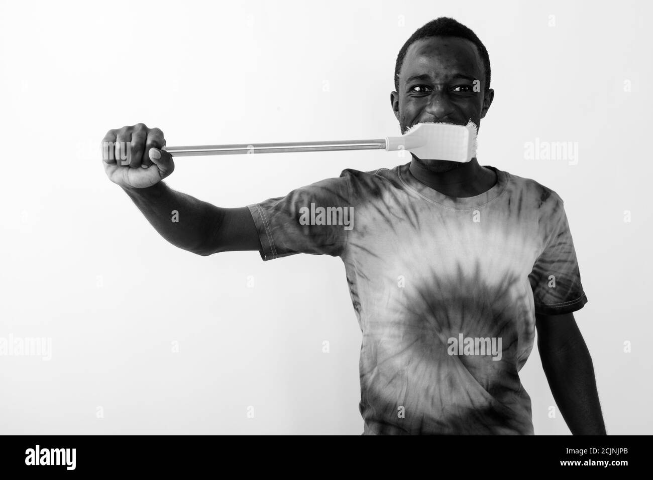 Studio shot of young black African man using big cleaning brush to brush his teeth against white background Stock Photo