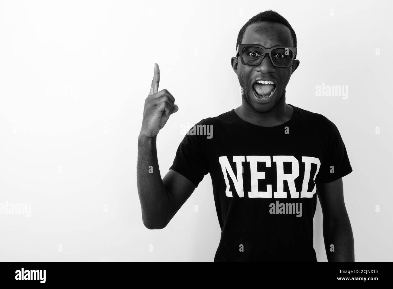 Studio shot of young happy black African geek man with great idea smiling and pointing finger up while wearing Nerd shirt Stock Photo