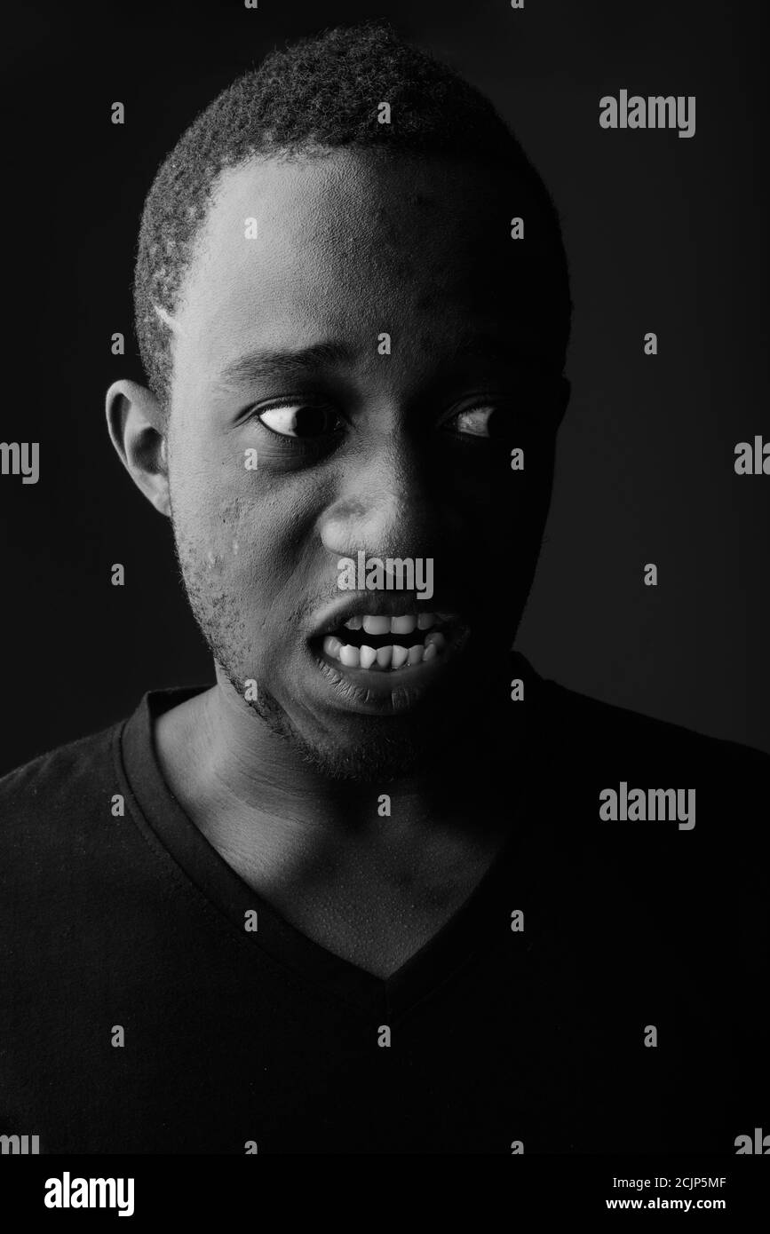 Studio shot of angry young black African man screaming in dark room Stock Photo