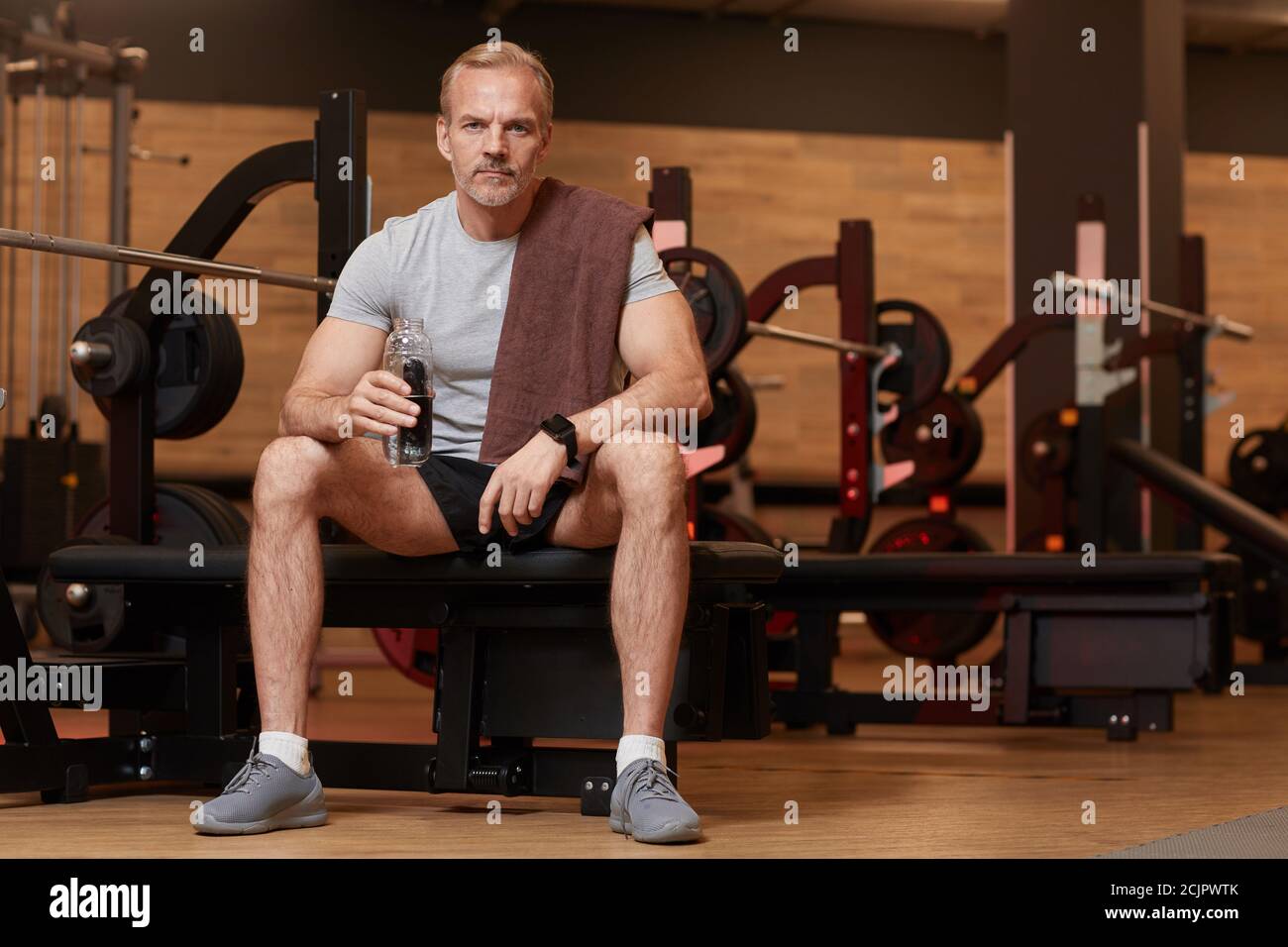 Portrait of mature man drinking water and looking at camera while sitting and resting after sports training Stock Photo